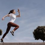 Athletic woman running on an outdoor road, demonstrating fitness and determination under a blue sky.