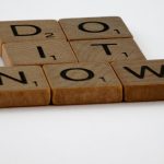 Wooden Scrabble tiles spelling 'Do It Now' on a white background. Motivational concept.